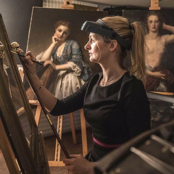 Sally holds a paintbrush in her hands and works on an oil painting