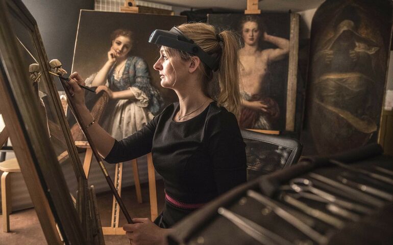 Sally holds a paintbrush in her hands and works on an oil painting