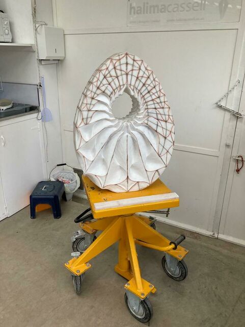 An egg shaped white marble sculpture with a hole where the yolk would be, it has been carved with red geometric patterns