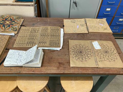 Four sketchbooks filled with geometric designs are laid out open on a table