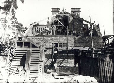 A black and white photograph of Limnerslease being constructed by hand, the photograph features men working hard on the roof of the building
