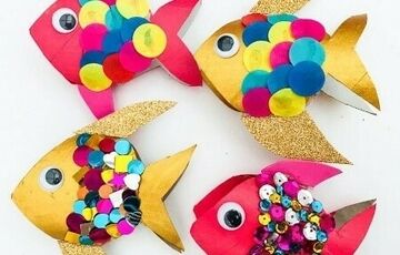 Four colorful paper fish crafts decorated with sequins, googly eyes, and multicolored paper circles on a white background.
