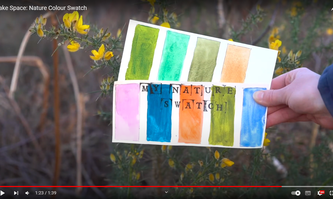 A hand holding a swatch book titled "my nature swatch" featuring various watercolour patches in shades of green, orange, pink, and blue, against a background of yellow flowers.