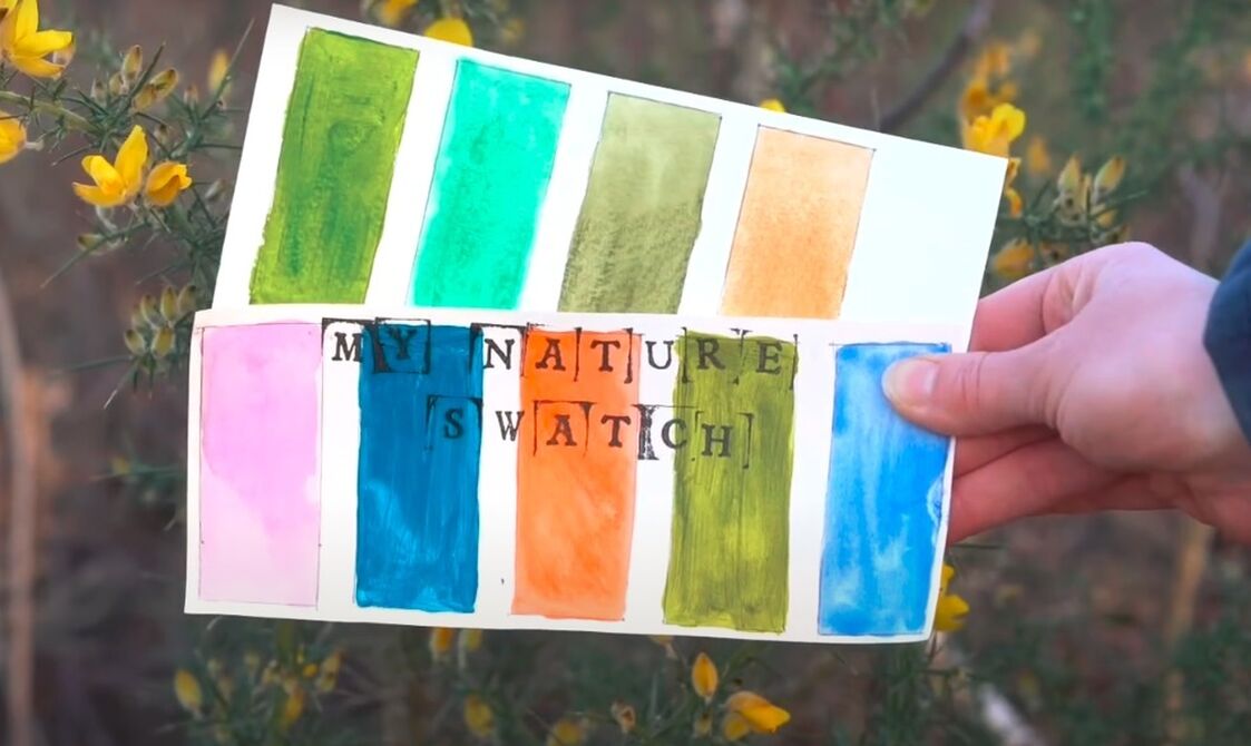 A hand holding a swatch book titled "my nature swatch" featuring various watercolour patches in shades of green, orange, pink, and blue, against a background of yellow flowers.