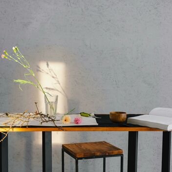 A wooden table with a book, paper, paints and a flower in a glass placed on top
