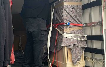 A man securing a wooden crate inside a van with straps