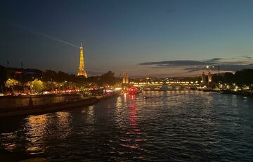 A nighttime view of the River Seine in Paris, with the Eiffel tower lit up in the distance