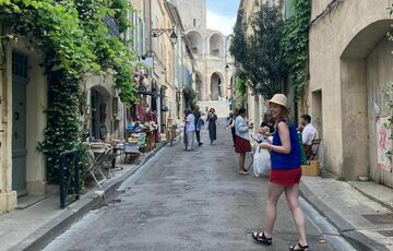 A woman with red shorts and a blue top walks down a narrow street in Arles surrounded by jasmine