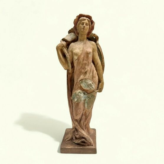 A graceful art nouveau terracotta statue of a woman, possibly a nymph or goddess, in shades of reddish-brown and muted green. She stands draped in fabric, holding large leaves, with a serene expression.