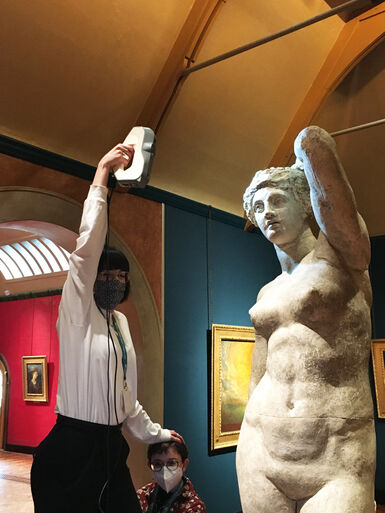 A curator holds their arm up with scanner by plaster sculpture