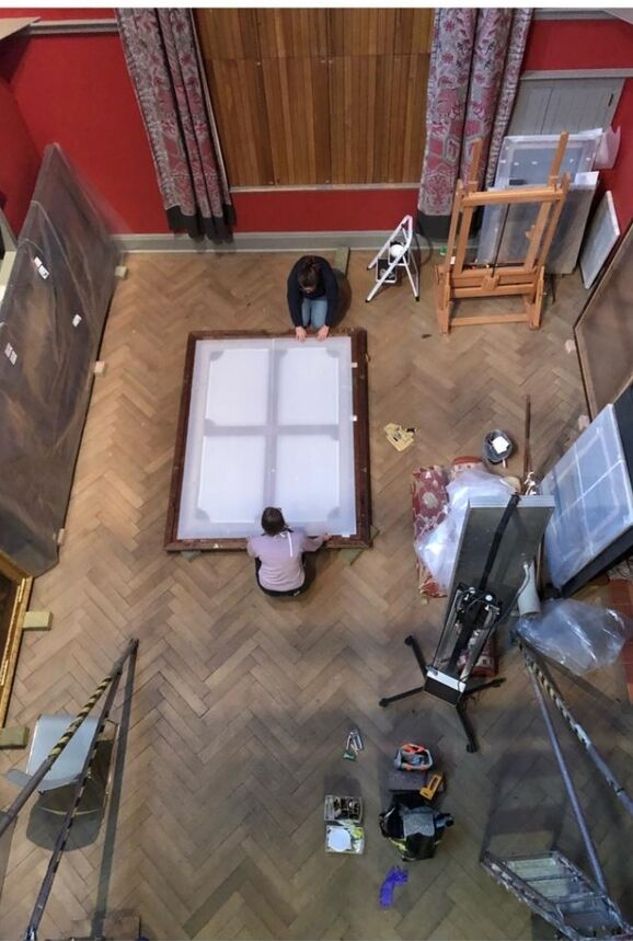 two figures frame a painting on the floor