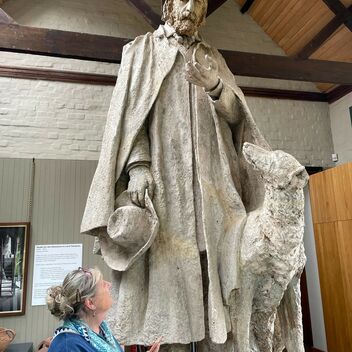 Jenny holds a phone and looks up at large sculpture of Tennyson
