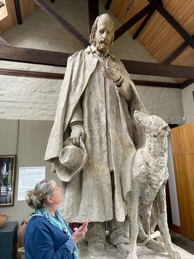 Jenny holds a phone and looks up at large sculpture of Tennyson