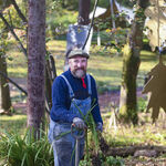 Chris holds a spade and is surrounded by plants