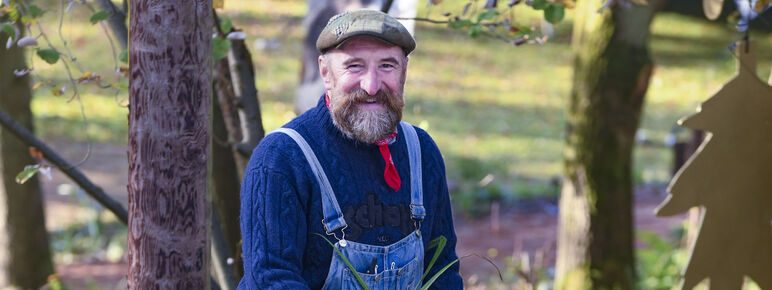 Chris holds a spade and is surrounded by plants