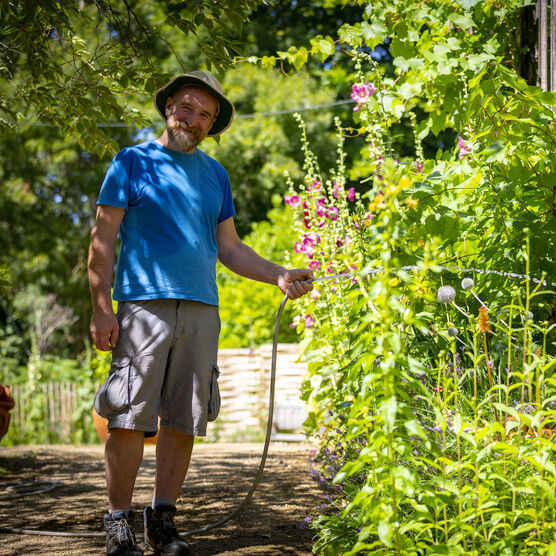 Chris smiles to the camera and waters flowers with hose