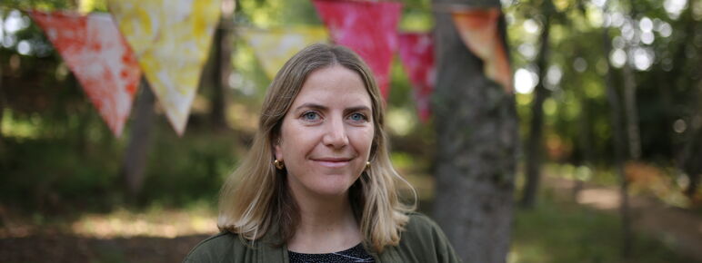 Sarah smiles to camera in woodlands with bunting behind her