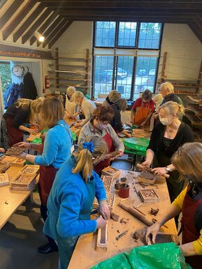 A group of people stand at tables making clay tiles