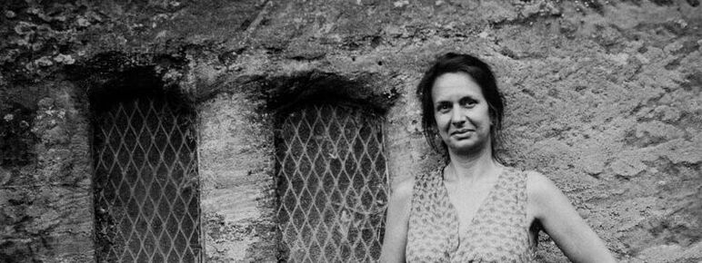 Black and white tintype portrait of a woman standing by an old stone wall