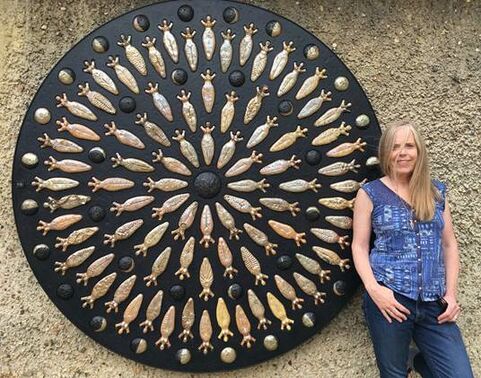 A women stands next to a circular artwork in black and bronze colours