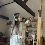 Sarah wears headphones and works on a painting on an easel