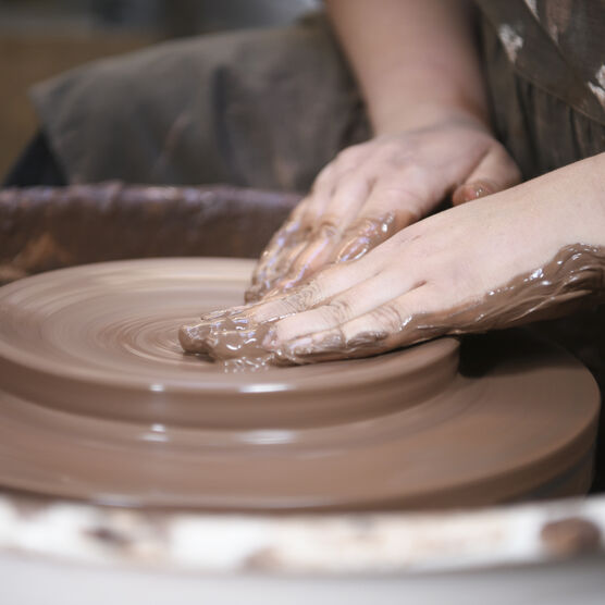 A close up of Ashleigh shaping clay on a pottery wheel