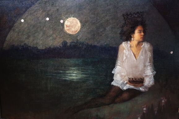 A woman sits by a river underneath a bridge, she wears a white blouse and there is a dark crown on her head. The full moon is visible behind her over the river