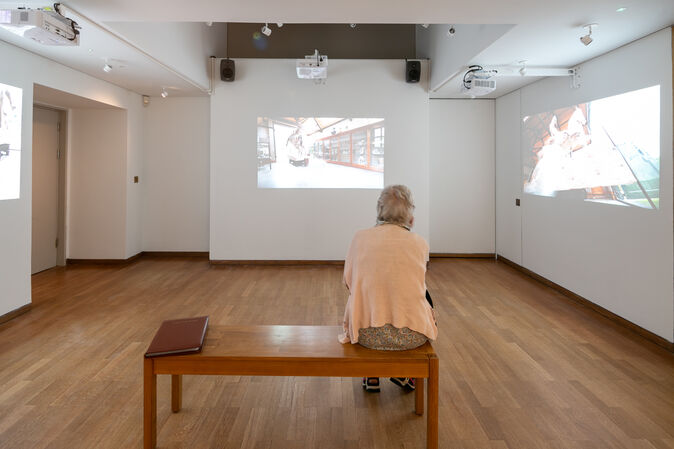 A visitor sits on a bench and watches the video installation