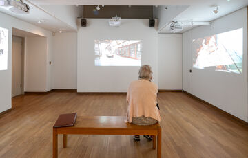 A visitor sits on a bench and watches the video installation