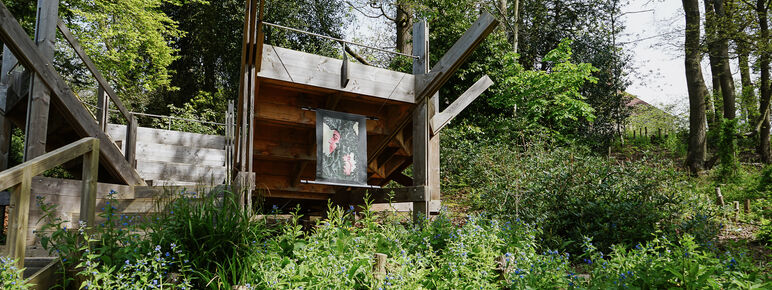 Photo of Bench 1 in the Limnerslease woodland at Watts Gallery with a painting displayed on the side of two side profile faces