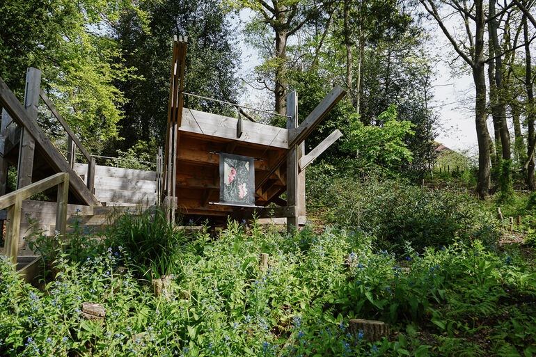 Photo of Bench 1 in the Limnerslease woodland at Watts Gallery with a painting displayed on the side of two side profile faces