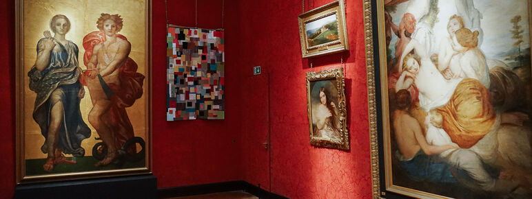 Photo inside the Historic Galleries at Watts Gallery. A multicoloured textiles artwork is hung beside a painting.