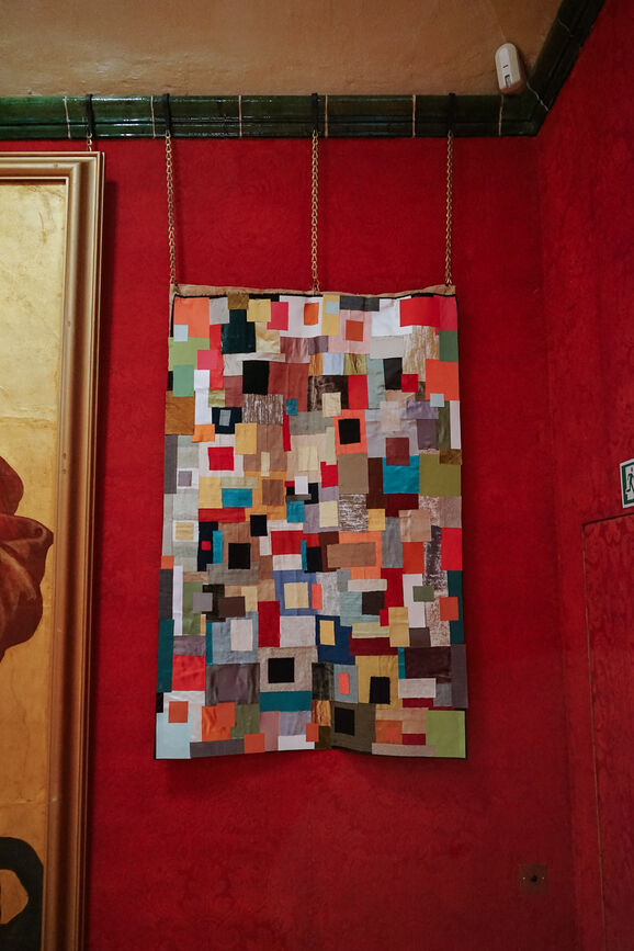 Photo inside the Historic Galleries at Watts Gallery. A multicoloured textiles artwork is displayed on the wall