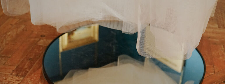 Photo inside the Historic Galleries at Watts Gallery. This is a close up image of the bottom of an installation hanging from the ceiling made from tulle with a mirror underneath