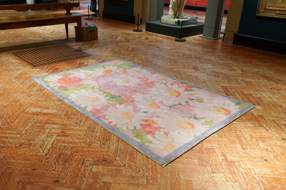 Photo of the floor of Watts Gallery with a rug placed in the middle of the image. The rug is decorated with a floral pattern