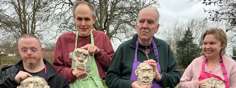 Four people holding their ceramic work and smiling at the camera