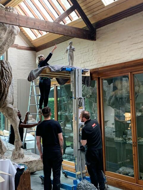 A group work on the sculpture gallery, one curator is on a ladder and points at a sculpture