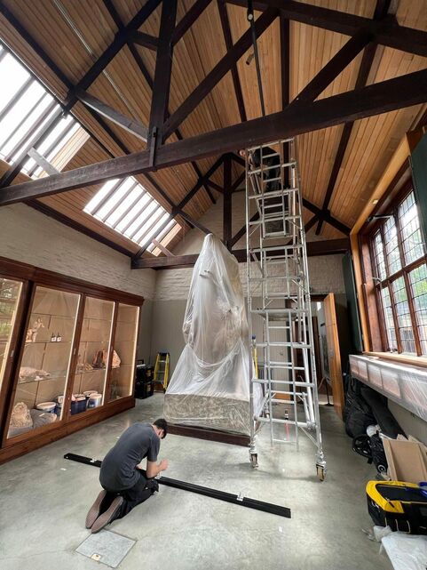 The Watts Sculpture Gallery under refurbishment. The Tennyson statue is covered in tarp and a ladder is set up next to it. A man crouches on the floor