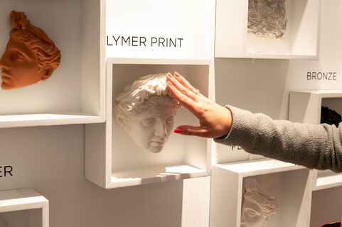 A hand touches a model of a sculpture, made from polymer print