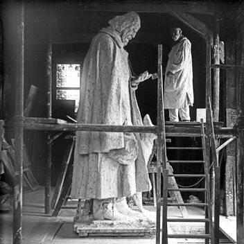 Black and white photo of artist G F Watts on scaffolding next to large statue of Lord Tennyson