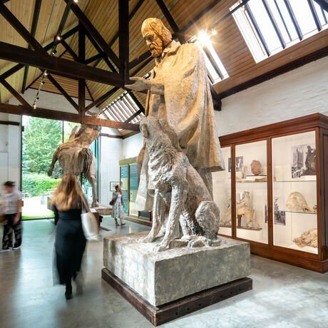 Visitors walk through tall ceiling gallery full of large sculptures