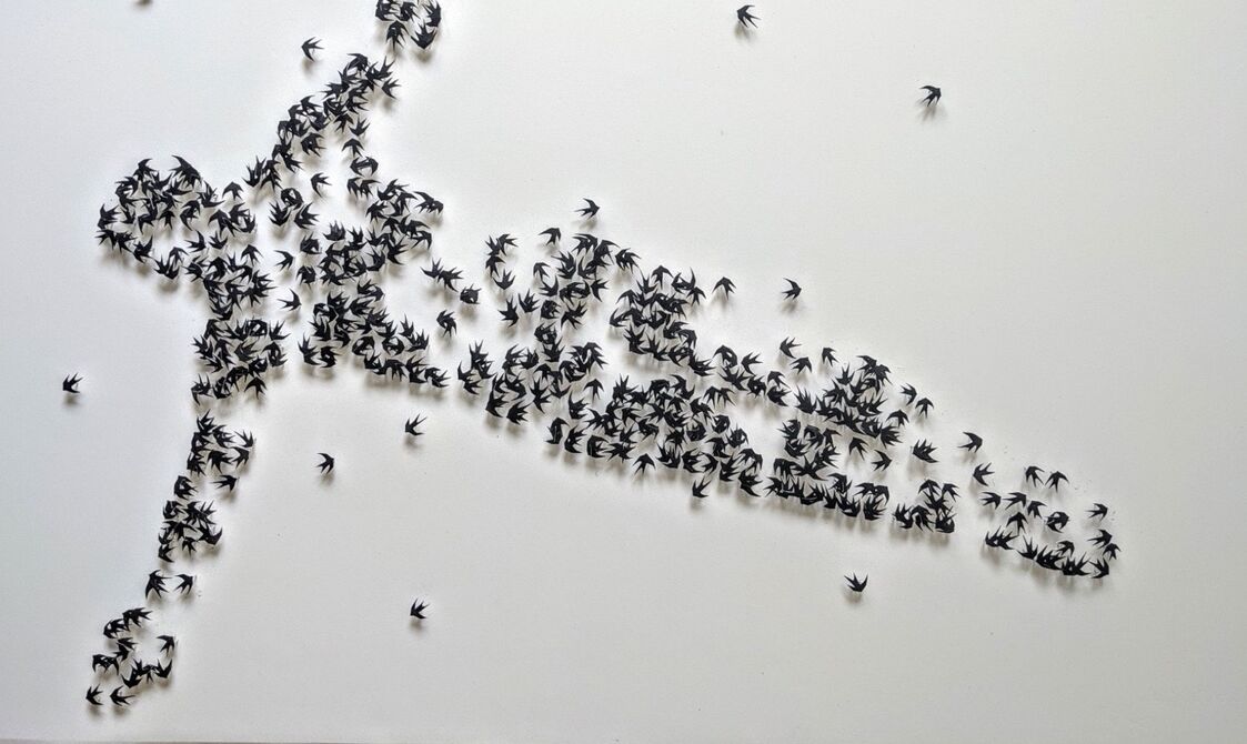 A form of a figure as if in flight created out of small- paper birds on pins