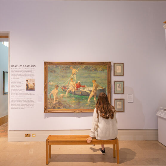 A visitor sits on a bench in front of a large beach scene painting