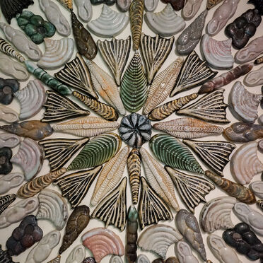 Photo of a ceramic tile installation by Kay Aplin. It features abstract shaped tiles in a mandala pattern