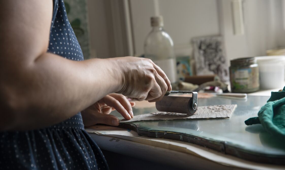 Lisa rolls ink over a piece of lino with a paint roller