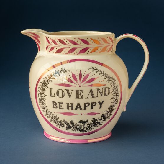 A cream jug embossed with the words 'love and be happy' in black print and floral pink and black designs surrounding it