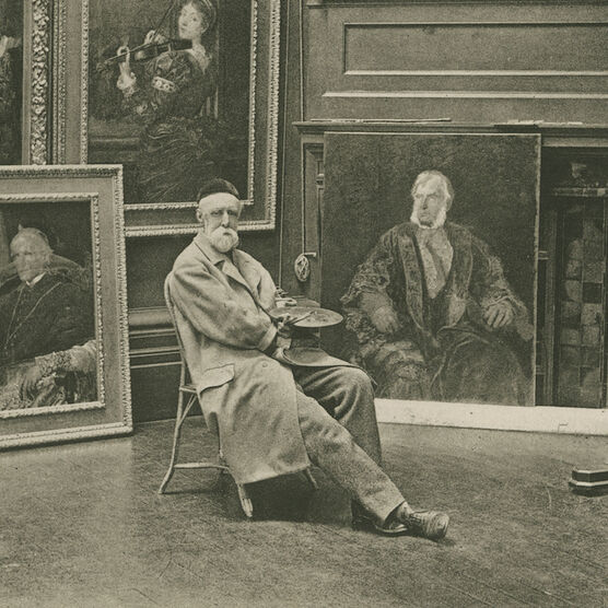 George sits on a chair surrounded by many framed paintings on the wall