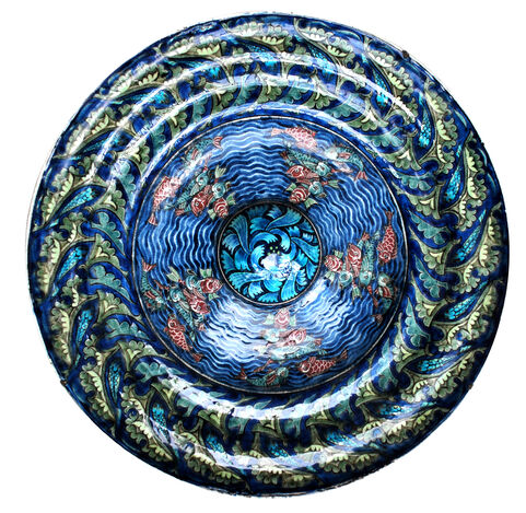 Tin glazed earthenware wide rimmed rice dish. In this intricately patterned dish red and green fish swim in swirling seas around a central petal boss. A seaweed pattern adorns the rim.