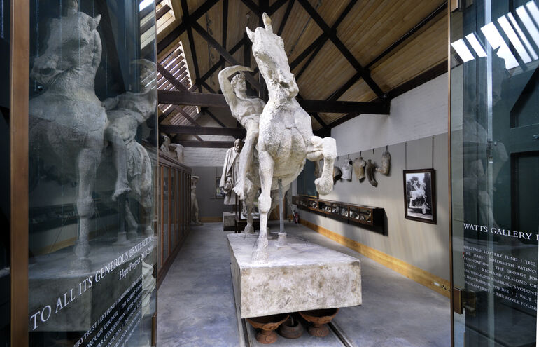 Statue of a man on a rearing horse seen through the galss doors of Watts Gallery