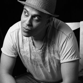 A photograph of Des Oliver, in black and white sitting on a chair